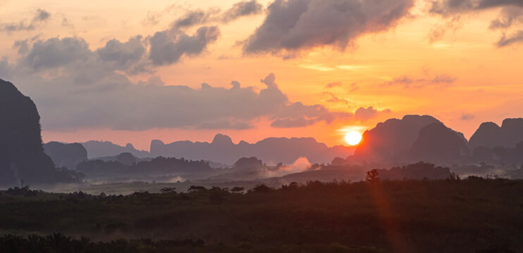 Beautiful sunrise landscape background with clear sun disk rising behind limestone karst mountains and pastel orange sky for travel design
