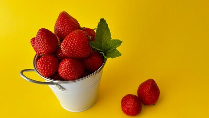  Fresh red strawberries with mint leaf in a small metal bucket on a bright yellow background © LD