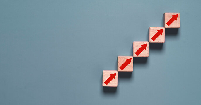 Wooden blocks with upward arrows arranged as ascending steps symbolize business growth, career advancement, success strategy, goal achievement, continuous improvement, progress and development.
