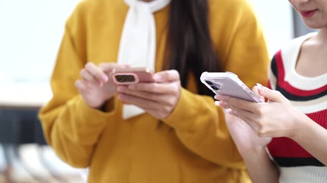Close-up of two young women's hands holding and using smartphones, typing and scrolling on screens. Lifestyle, technology, and social media concept.