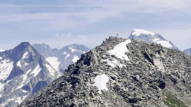 Hikers standing by a summit cross atop a jagged rocky ridge