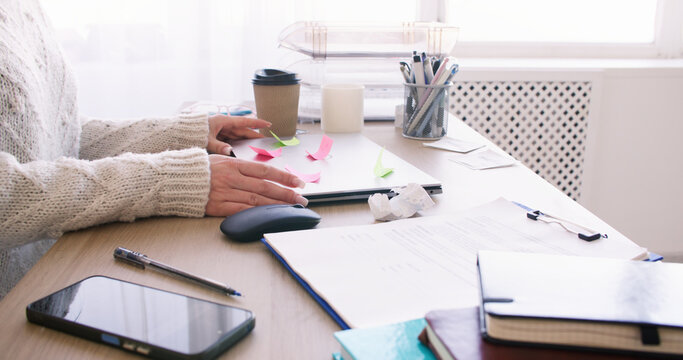 Online learning. Home study. Unrecognizable woman professional working at desk at workplace with laptop sticky notes smartphone indoor.