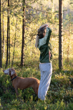 Exploring nature, healthy living and local tourism, woman accompanied by domestic dog walk in forest, female hiker with raised arms relaxing while observing landscape in woods, fresh air therapy.