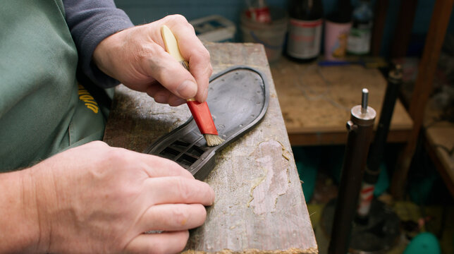 Shoemaker working. Cobbler workshop. Unrecognizable man professional expert hands applying glue for sole using brush at workplace.