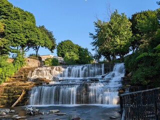 Naklejka premium Scenic multi-tiered waterfall cascading over stone ledges surrounded by green trees in summer