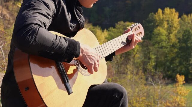 Portrait of smiling caucasian artist plays wooden acoustic guitar in autumnal park. Young songwriter plays string musical instrument hobby outside in nature fall time. Audio music healing in natural