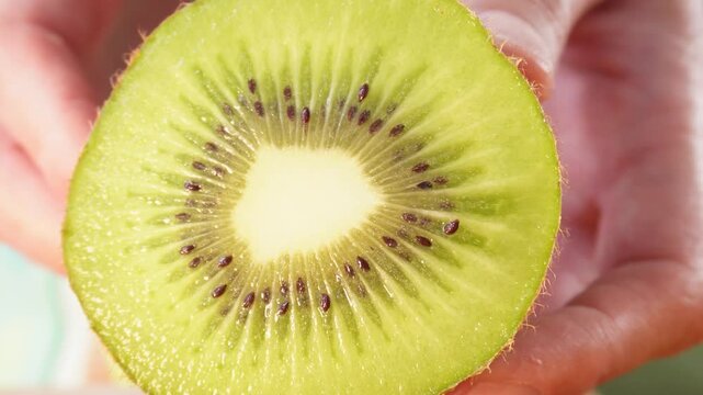 Fresh kiwi sliced, vibrant green flesh, tiny black seeds. Hands gently display fruit, inviting viewers to taste its juicy interior. Fruit's texture and color suggest health, natural goodness