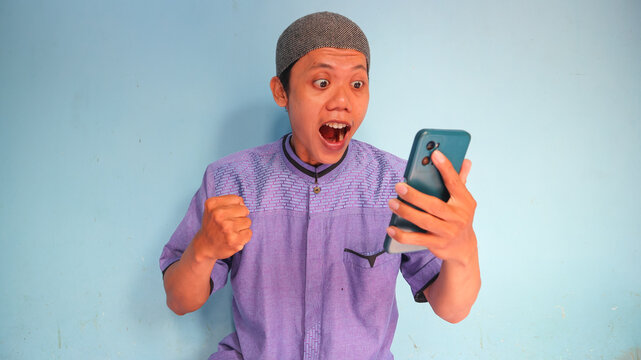 Asian Muslim man holding a cellphone with a happy expression