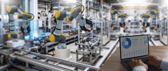 Fototapeta premium Hands type on a laptop dashboard showing industrial data while robotic arms run factory automation for manufacturing control, production monitoring, process analysis, and operations management.