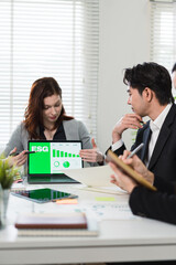 Business professionals discussing ESG performance metrics on a laptop screen during a corporate...