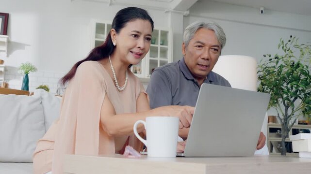 Senior spouses using laptop together sitting on couch at home. Elderly couple, hug and love on sofa with happy marriage, support and conversation of retirement home