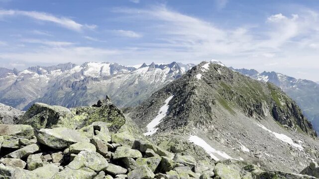Rocky alpine ridge with patches of snow leading to a peak above