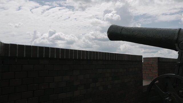 Historic cast-iron cannon overlooking a brick fortress wall in Chernihiv, Ukraine, beneath a bright midday sky filled with large white clouds.