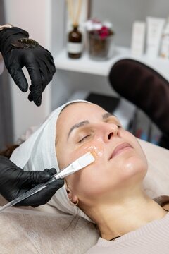 Beauty face. Moisturizing procedure. Cosmetician hands in gloves with hydrating gel for female client using brush in professional salon.