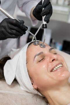 Cosmetologist salon. Lifting therapy. Female in black gloves using modern device for professional microcurrent face at spa workplace.