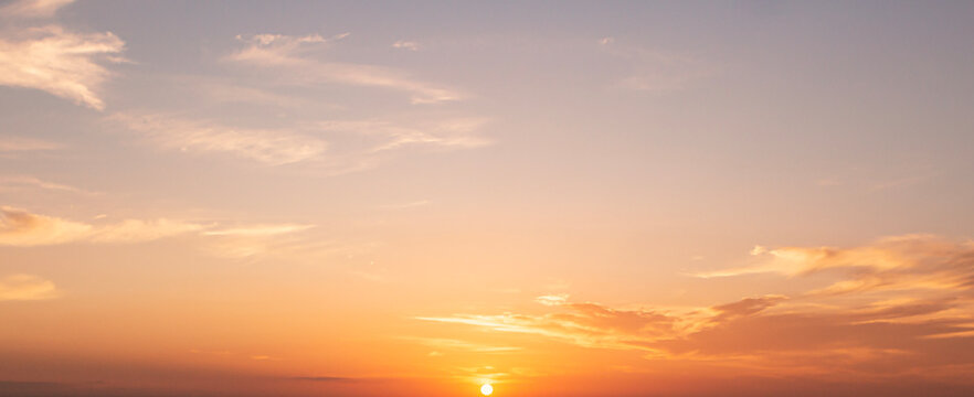 Beautiful sunset sky background with small sun disk on horizon and soft pastel orange pink clouds for panoramic travel mockup design