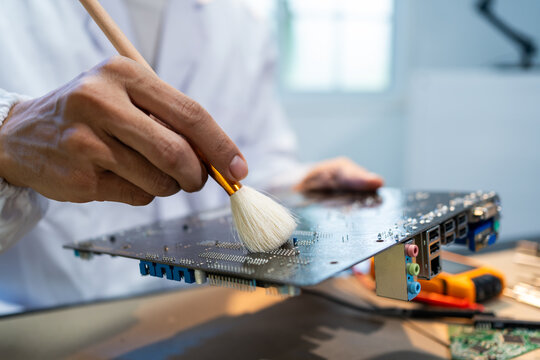 Close-up of a technician cleaning dust from a computer circuit board with a soft brush in a repair workspace, showing careful hardware maintenance and electronics service.