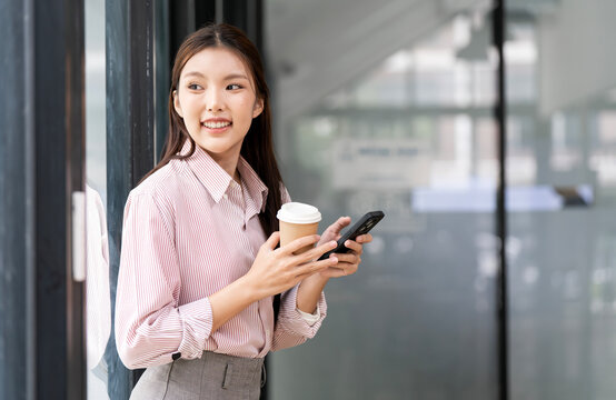 Smiling Young Asian Businesswoman with Coffee and Smartphone Outside Office