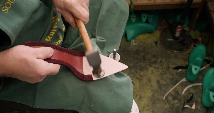 Cobbler workshop. Shoemaker working. Unrecognizable experienced man hands using footgear nailing with metal hammer for manufacturing.
