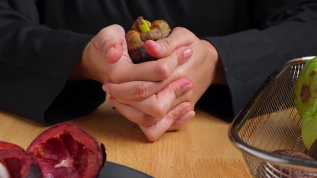 Hands squeezing open a Mangosteen, tropical and exotic fruit