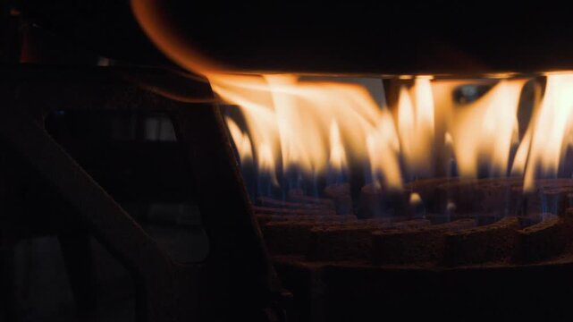 A close-up shot of an industrial gas stove burner with intense blue and orange flames heating a metal pot, highlighting the professional kitchen cooking environment