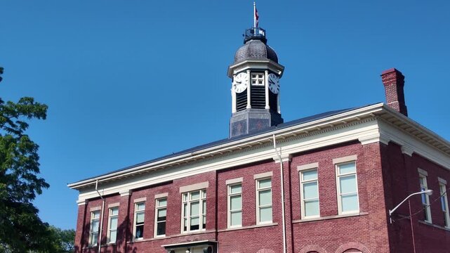 Historical red brick municipal building in Port Hope, Ontario, Canada with a central clock tower and manicured lawn.