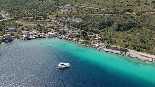 Panoramic aerial view of coastal fishing village Limeni on Mani peninsula, Turquoise waterfront old stone house towers on steep lush green mountains on a sunny day, Mediterranean mountain vegetations