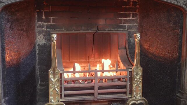 Traditional fireplace with bright flames burning in the Christ Church dining hall in Oxford, framed by ornate metal and brick.