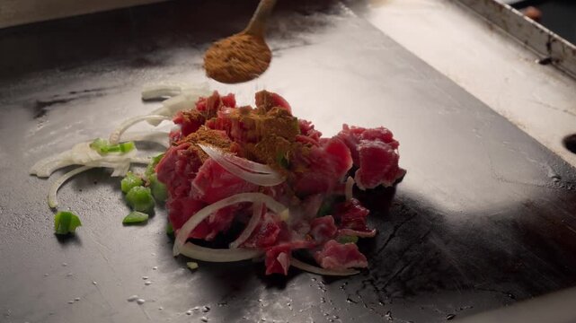 chef sprinkles spices on fresh meat, sizzles on a flat top hot griddle