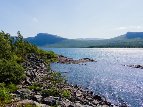 Scenic view of the river flowing through Stora Sj&ouml;fallet National Park with rocky shoreline, surrounding mountains and summer vegetation in Swedish Lapland. Landscape in the UNESCO World Heritage area