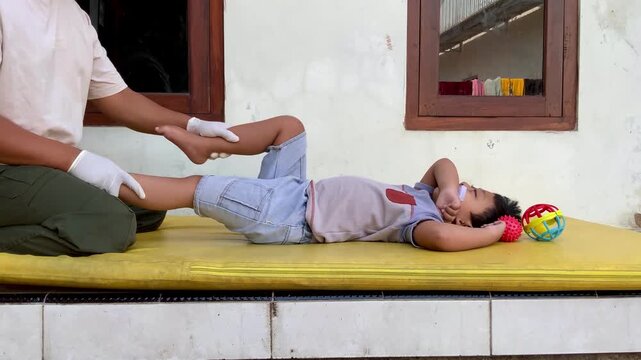 Father helping his young son with pediatric physical therapy leg stretching exercises at home