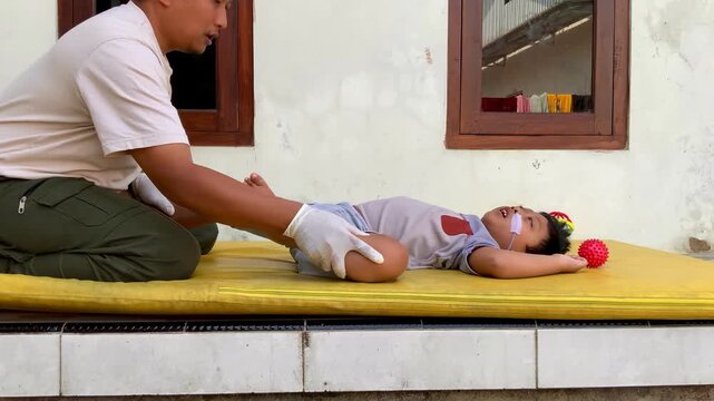 Father helping his young son with pediatric physical therapy leg stretching exercises at home