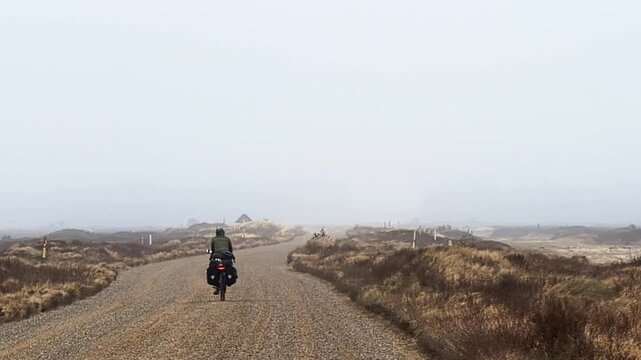 Cyclist bikepacking on a remote foggy road in Denmark