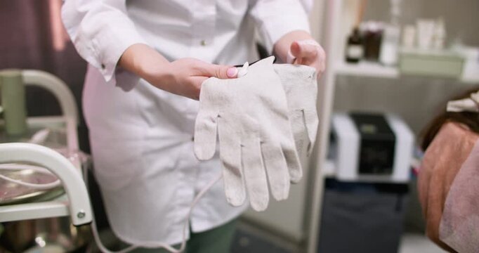 Microcurrent gloves preparing. Cosmetologist occupation. Unrecognizable female using modern device for beauty skin treatment in professional salon.