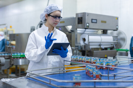 Female worker using tablet technology inside modern manufacturing factory checking safety equipment while wearing protective uniform near production line