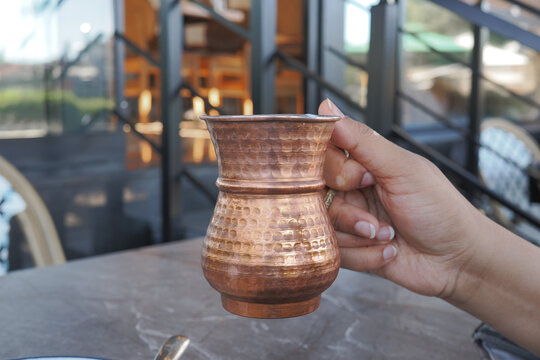A hand holds a copper ayran cup. a turkish drink