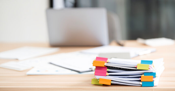 Stacked documents with colorful paper clips on office desk.