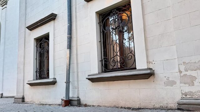 Historic building facade with elegant wrought iron window grilles and textured stone walls in soft daylight. Architectural exterior showcasing classic craftsmanship, urban heritage, and timeless desig