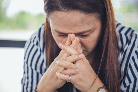 Depressed and stressed Asian middle-aged woman sitting lonely on a bench with head in hands inside an industrial background. Concept of financial crisis, business bankruptcy, debt pressure, mental hea