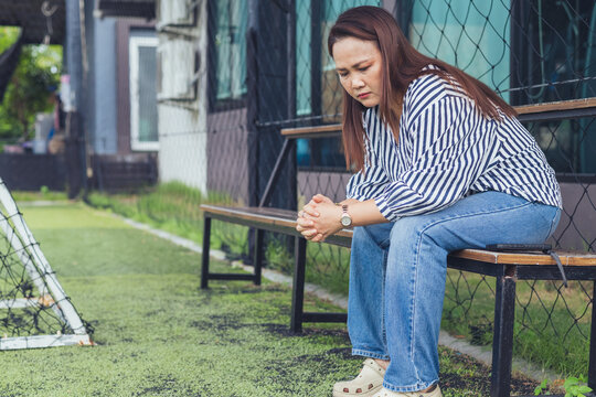 Sad and depressed Asian woman sitting lonely on a bench with anxious expression facing emotional stress. Concept of severe mental health crisis, chronic stress, depression, midlife crisis, personal pr