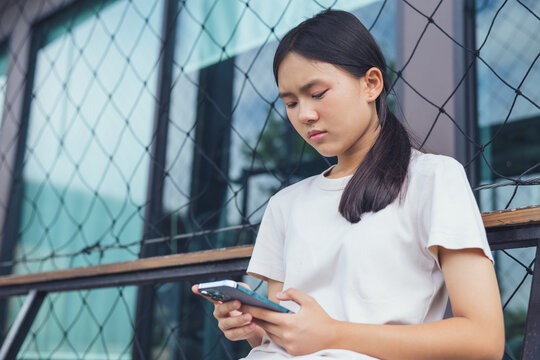Worried and stressed Asian teenager girl holding smartphone looking at screen with anxious expression. Concept of cyberbullying, social media peer pressure, smartphone digital addiction, and youth men
