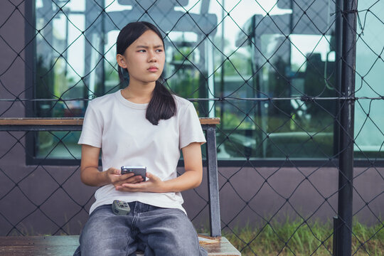 Worried and stressed Asian teenager girl holding smartphone looking at screen with anxious expression. Concept of cyberbullying, social media peer pressure, smartphone digital addiction, and youth men