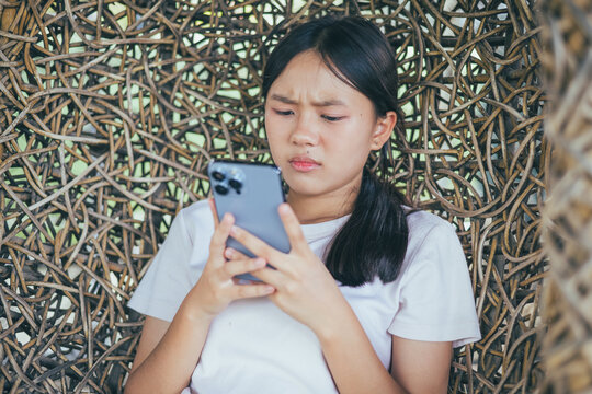 Worried and stressed Asian teenager girl holding smartphone looking at screen with anxious expression. Concept of cyberbullying, social media peer pressure, smartphone digital addiction, and youth men