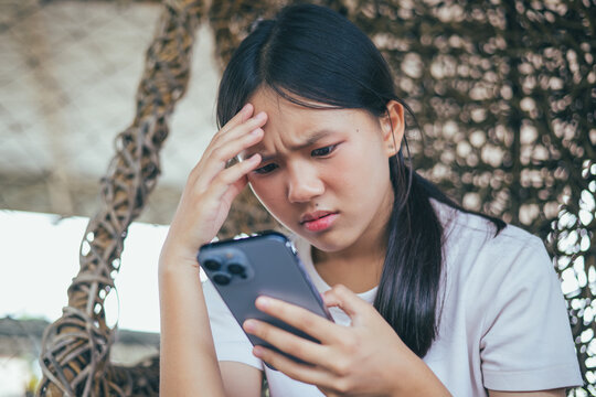Worried and stressed Asian teenager girl holding smartphone looking at screen with anxious expression. Concept of cyberbullying, social media peer pressure, smartphone digital addiction, and youth men