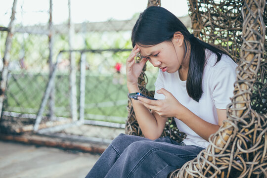 Worried and stressed Asian teenager girl holding smartphone looking at screen with anxious expression. Concept of cyberbullying, social media peer pressure, smartphone digital addiction, and youth men