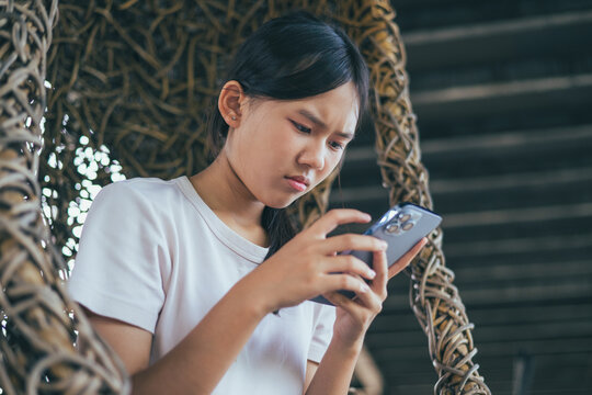 Worried and stressed Asian teenager girl holding smartphone looking at screen with anxious expression. Concept of cyberbullying, social media peer pressure, smartphone digital addiction, and youth men