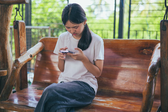 Worried and stressed Asian teenager girl holding smartphone looking at screen with anxious expression. Concept of cyberbullying, social media peer pressure, smartphone digital addiction, and youth men