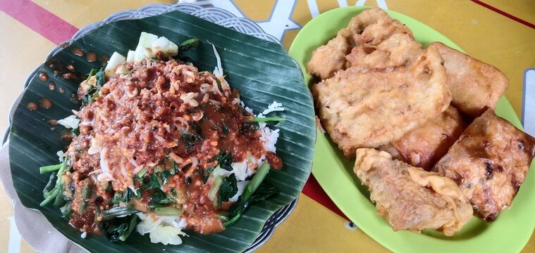 Traditional Indonesian pecel rice with peanut sauce and assorted fried snacks on banana leaf