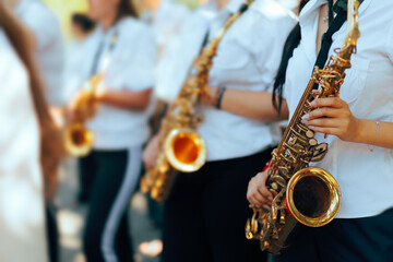 Obraz premium Female Saxophonists Playing Instruments Close Up In Marching Band. Group of young girls in uniform shirts holding golden saxophones during parade