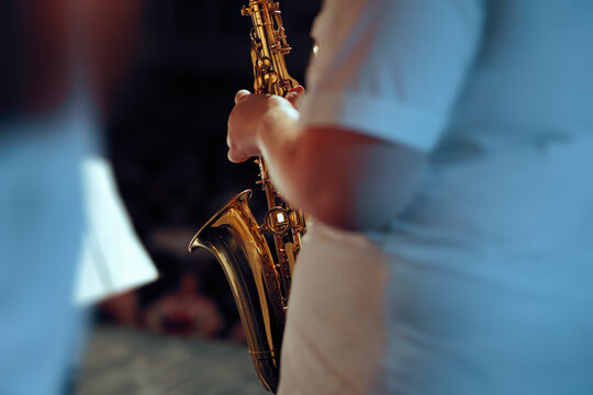 Musician Playing Saxophone Close Up Profile View During Concert. Saxophonist holding brass instrument close to face performing live on dark stage